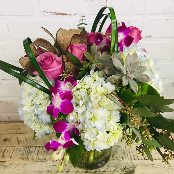 Pink roses and purple orchids arranged with white hydrangeas in a glass vase
