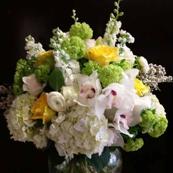 Mixed bouquet of white, yellow, and green flowers in a glass vase