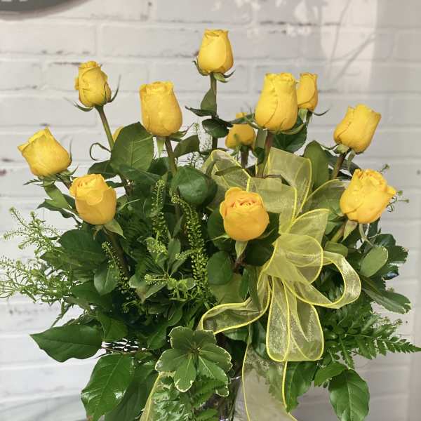 Yellow roses arranged in a clear glass vase with a yellow ribbon
