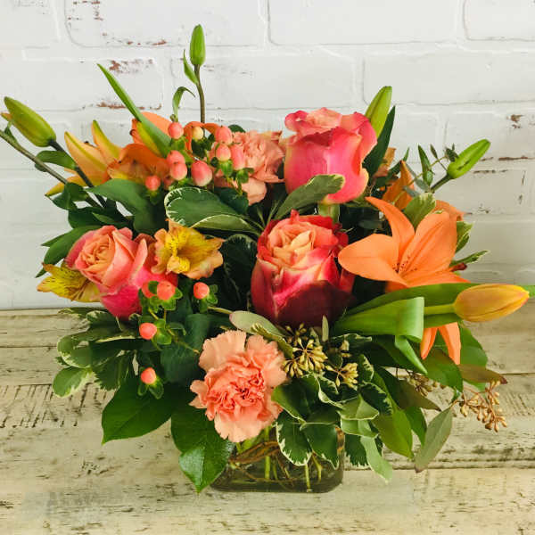 Mixed bouquet of pink roses, lilies, and carnations in a glass vase