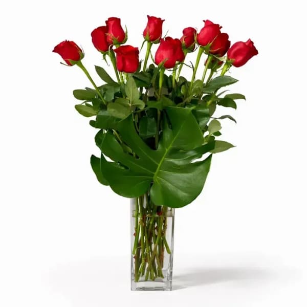 Red roses in a clear glass vase with large green leaves