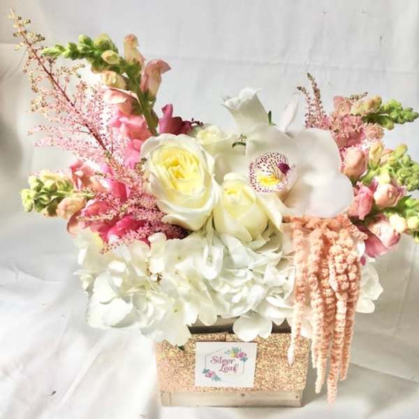 Pink and white floral arrangement in a glittery box with cascading blooms
