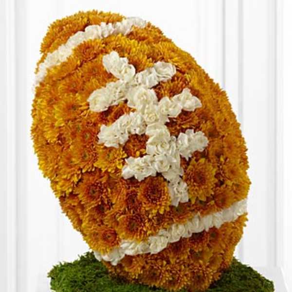 Football-shaped arrangement of orange flowers with white accents on a green moss base