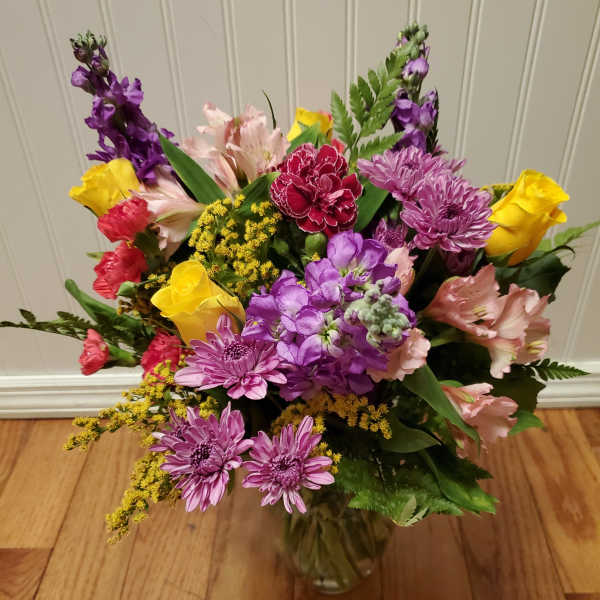 Mixed bouquet of yellow roses, purple mums, pink alstroemeria and carnations in a clear glass vase