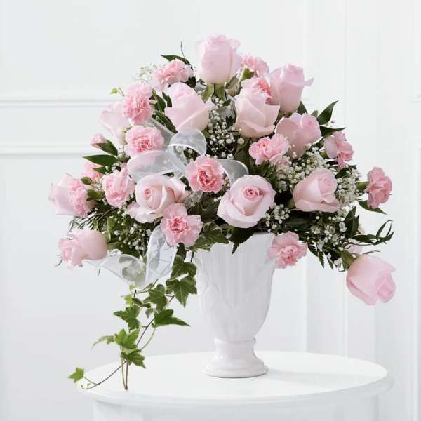 Pink roses and carnations in a white vase with a sheer ribbon