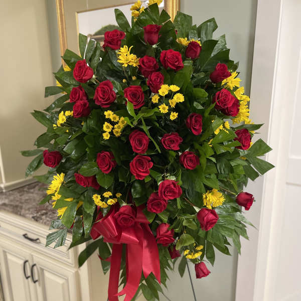Standing spray of red roses and yellow daisies with a red ribbon
