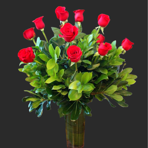 Red roses arranged in a clear glass vase with dense greenery