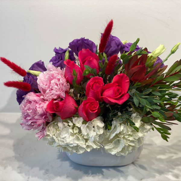Bouquet of pink roses, purple blooms, and white flowers in a white vase