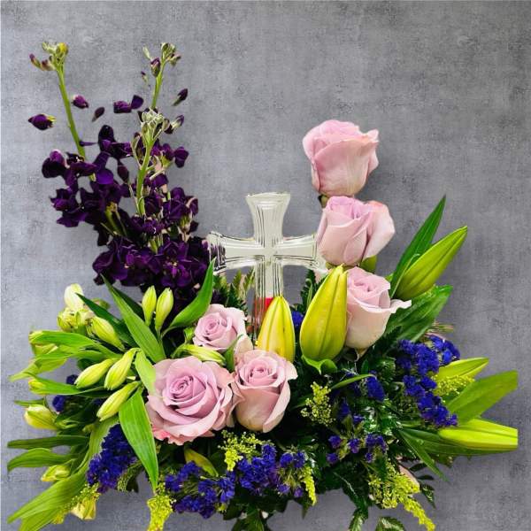 Pink roses and purple flowers arranged around a clear cross centerpiece