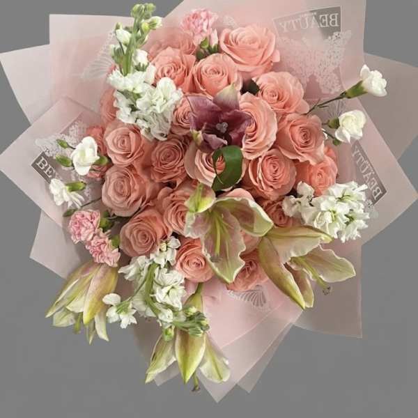 Hand-tied bouquet of peach roses, white blooms, and lilies wrapped in pink paper