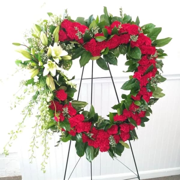 Heart-shaped floral wreath with red carnations and white lilies on a stand