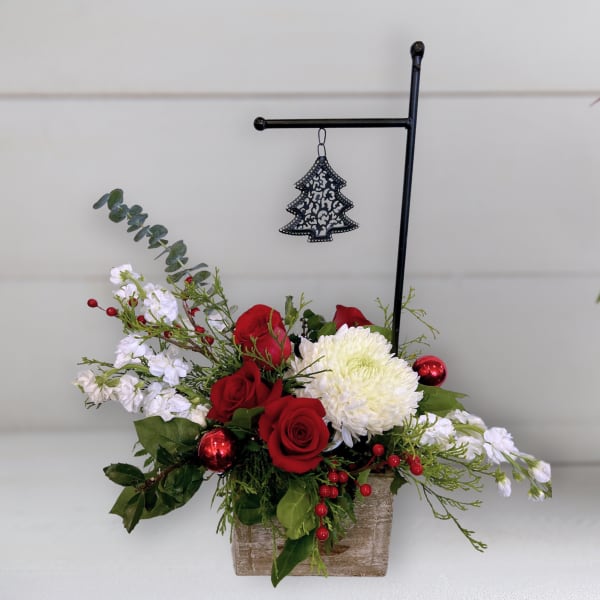 Red roses and white blooms in a rustic wooden container with a hanging tree ornament