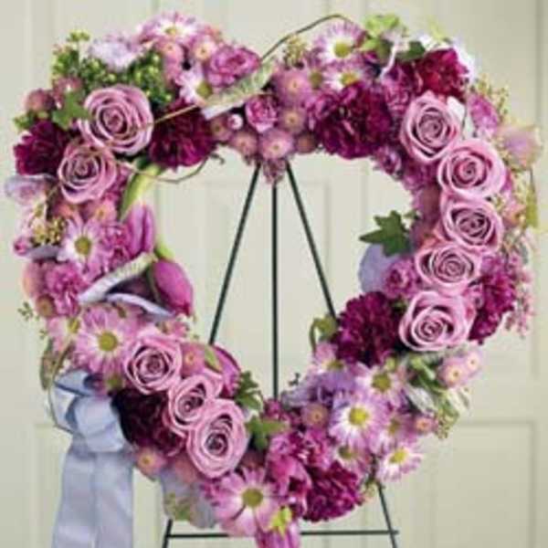 Heart-shaped floral wreath with pink roses and daisies on a stand