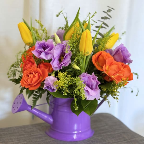 Bouquet of orange roses, purple lisianthus, and yellow tulips in a purple watering can