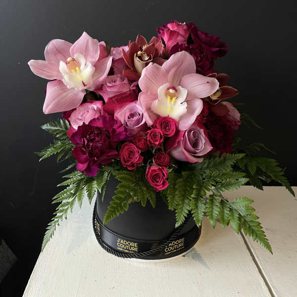 Pink orchids and roses arranged in a black hat box