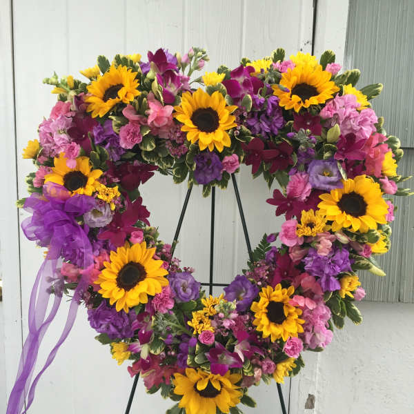 Heart-shaped floral wreath with sunflowers, purple and pink blooms, and a ribbon