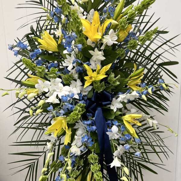 Tall standing floral spray with yellow lilies, white orchids, and blue flowers