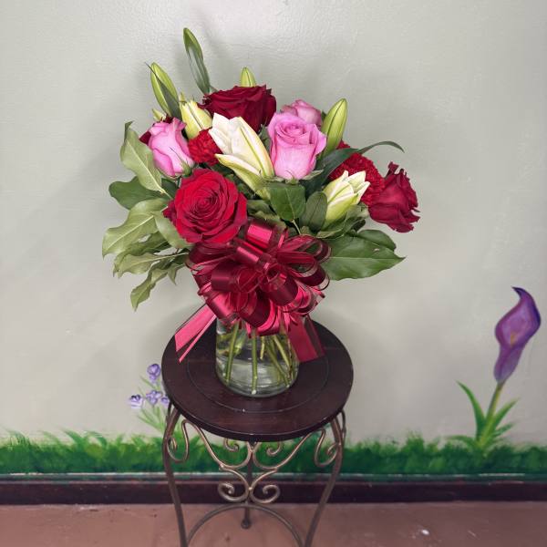 Mixed bouquet of red and pink roses with white lilies in a clear glass vase with a red bow.
