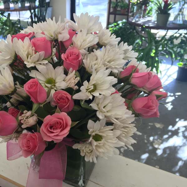 Pink roses and white daisies arranged in a clear vase with a pink ribbon.