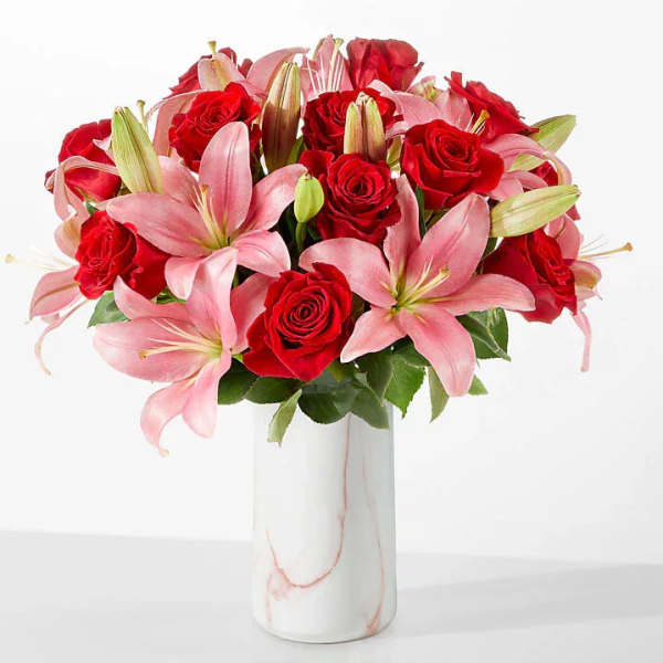Pink lilies and red roses arranged in a white vase