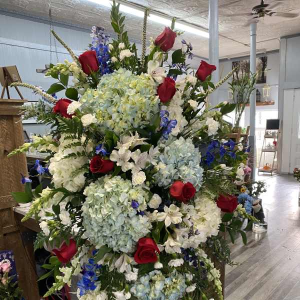 Large standing floral spray with red roses, blue hydrangeas, and white blooms