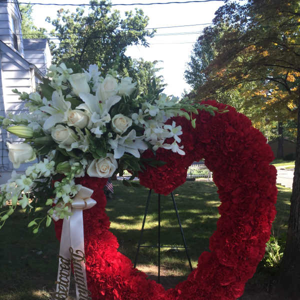 Heart-shaped floral wreath with red and white flowers on an outdoor stand