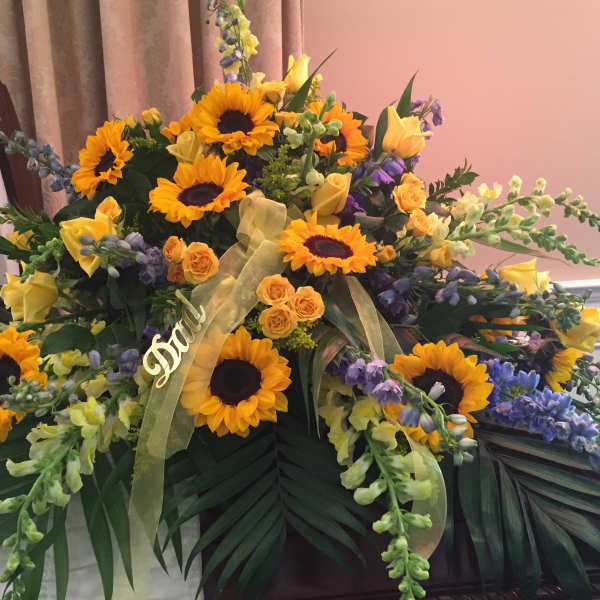 Large funeral spray with sunflowers, yellow roses, and purple flowers