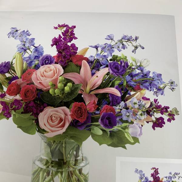 Mixed bouquet of pink, purple, and blue flowers in a clear glass vase