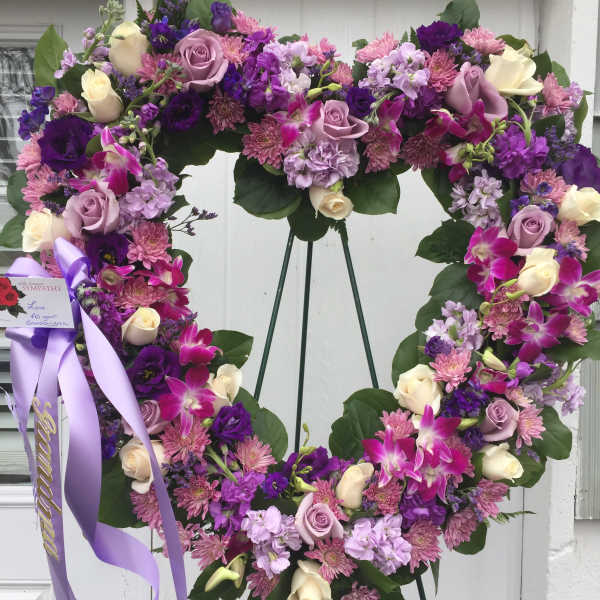 Heart-shaped floral wreath with purple, pink, and cream flowers on an easel