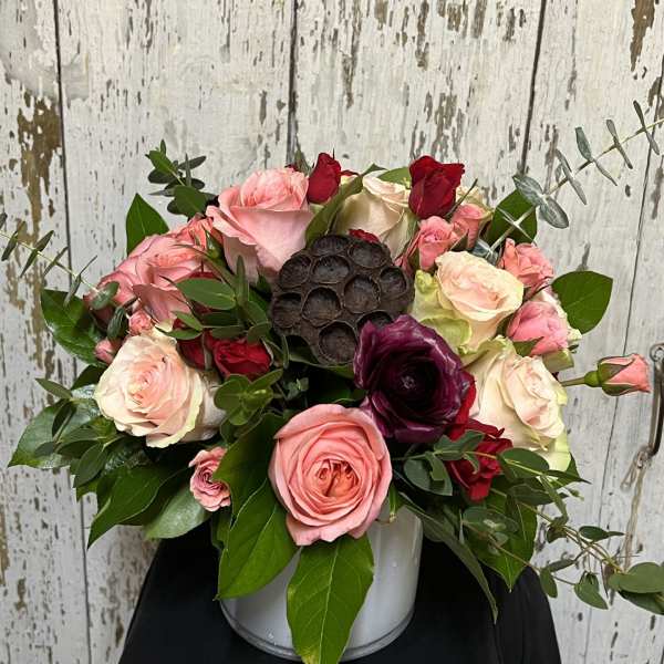 Pink and cream roses arranged in a white container with dark accent blooms