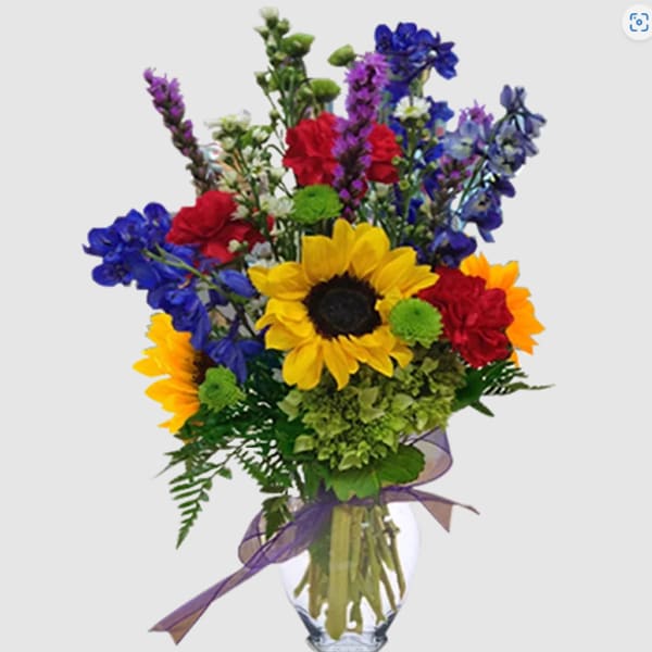 Colorful bouquet with sunflowers, red carnations, and blue flowers in a glass vase