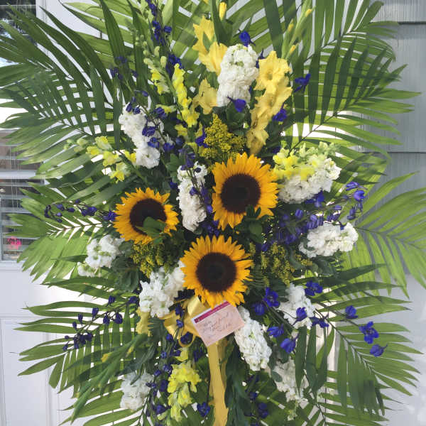 Large standing floral spray with sunflowers, white blooms, and palm fronds