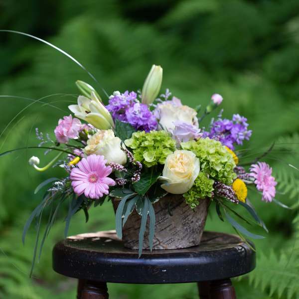 Mixed bouquet in a rustic container with pink, purple, white, and green blooms