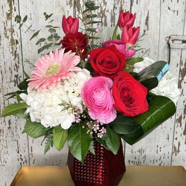 Mixed bouquet of red, pink, and white flowers in a red vase