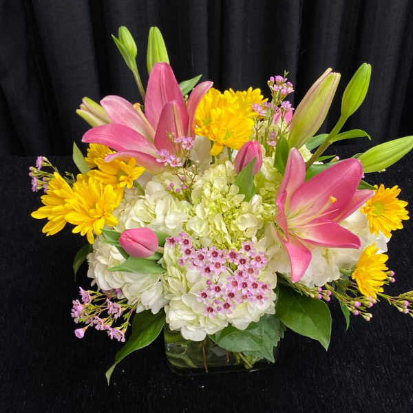 Pink lilies and yellow daisies arranged with white hydrangeas in a glass vase
