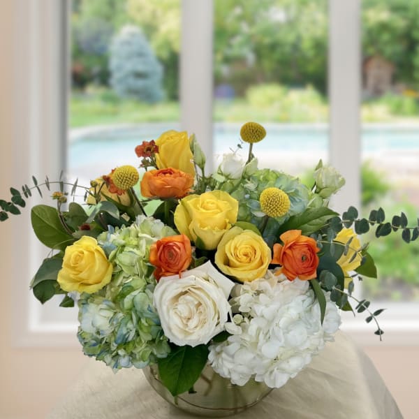 Yellow and orange roses with white hydrangeas in a glass bowl vase