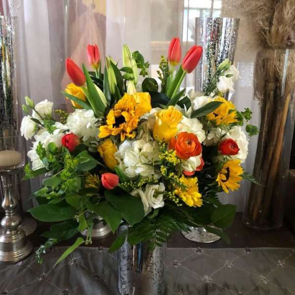 Mixed bouquet with tulips, roses, sunflowers, and white blooms in a silver vase
