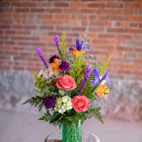 Colorful mixed bouquet in a green vase on a wooden stool