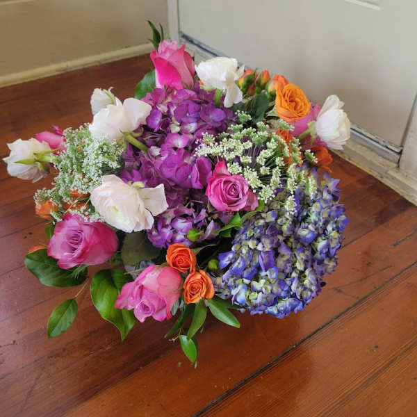 Mixed bouquet of pink, purple, white, and orange flowers on a wooden floor