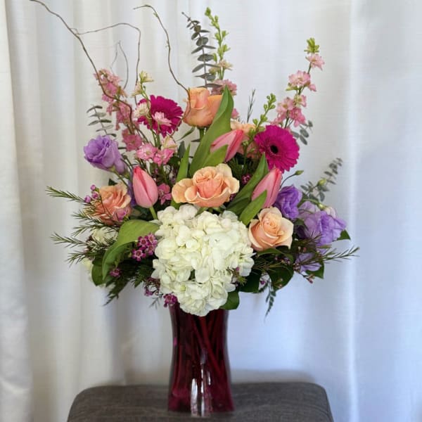 Mixed bouquet in a tall burgundy vase with pink, peach, purple, and white flowers