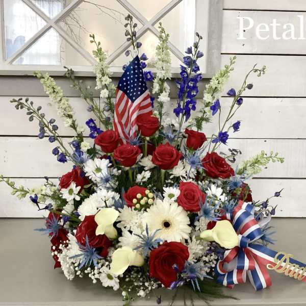 Red roses and white flowers arranged with an American flag and ribbon