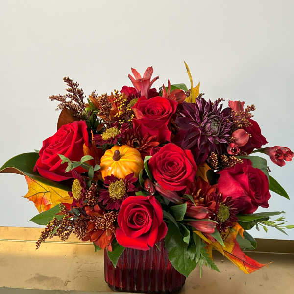 Red roses and autumn flowers in a red glass vase with a small pumpkin