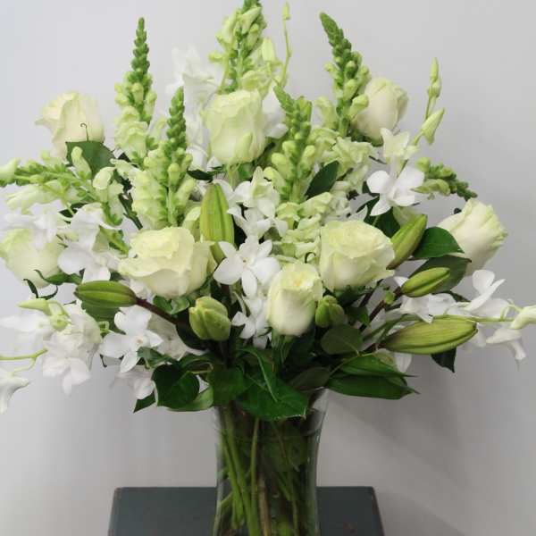 Tall arrangement of white roses, lilies, orchids, and snapdragons in a clear glass vase