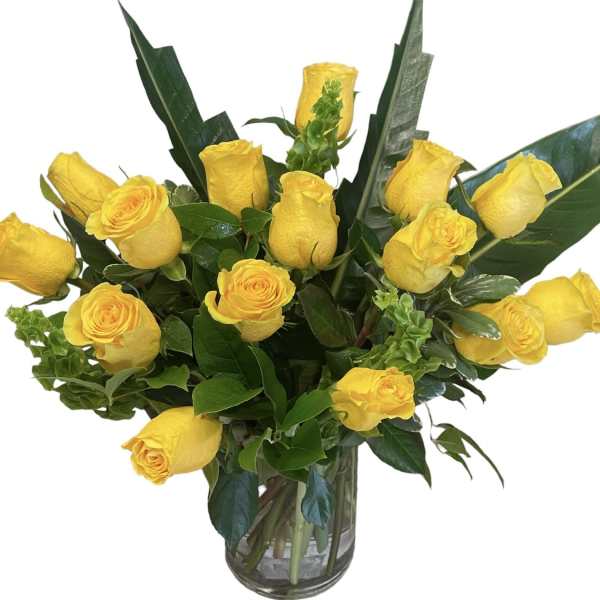 Yellow roses arranged in a clear glass vase with broad green leaves