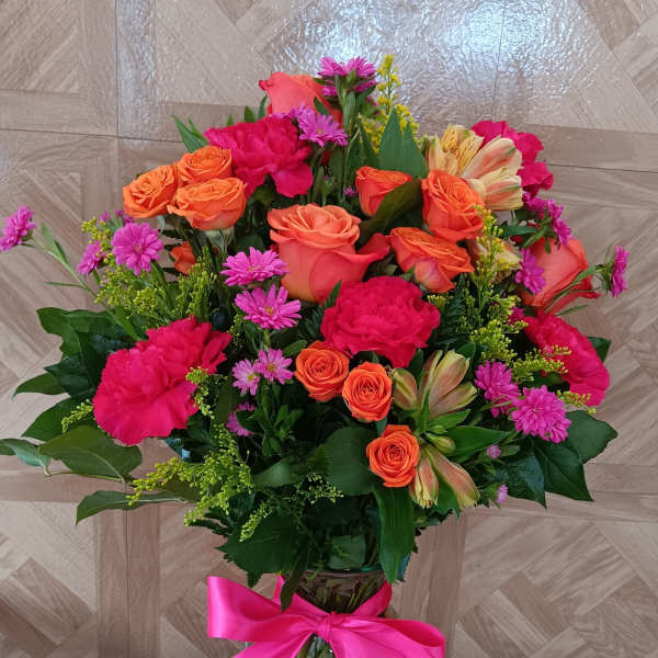 Tall vase arrangement of bright orange roses and hot pink flowers with a pink bow.