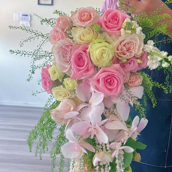 Handheld bouquet of pink and cream roses with pale orchids