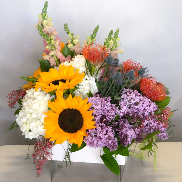Bright mixed bouquet with sunflowers, hydrangeas, and purple lilacs in a white container