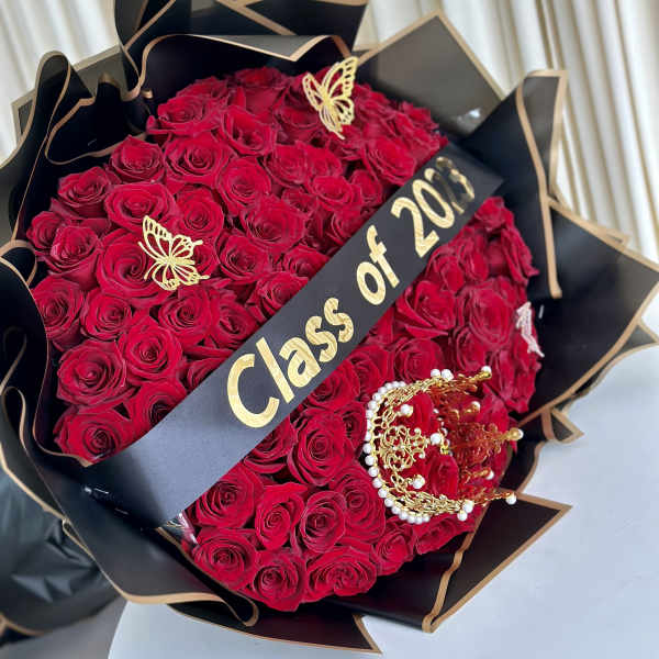 Large bouquet of red roses wrapped in black paper with gold butterflies, crown, and Class of 2023 banner
