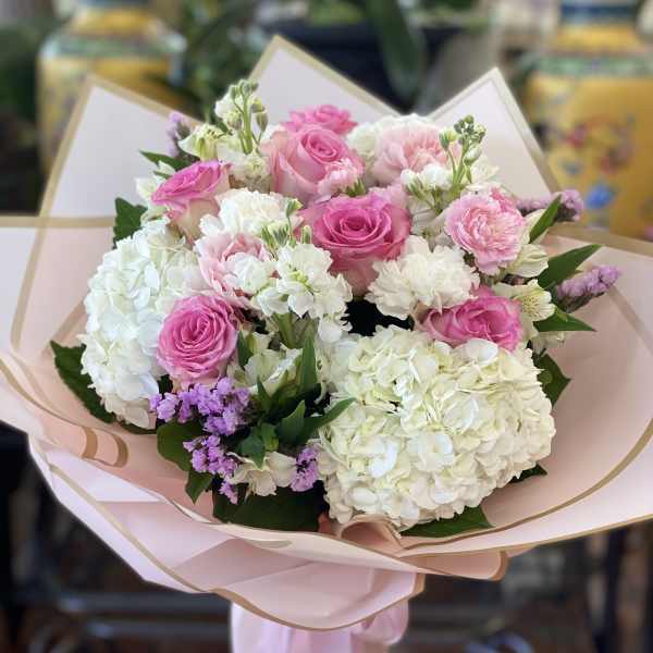 Pink and white bouquet of roses, hydrangeas, and carnations wrapped in blush paper