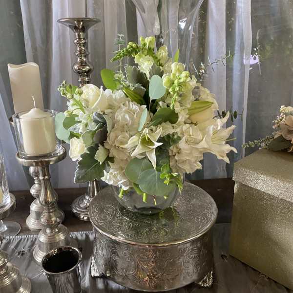 White floral centerpiece in a glass vase on a silver stand
